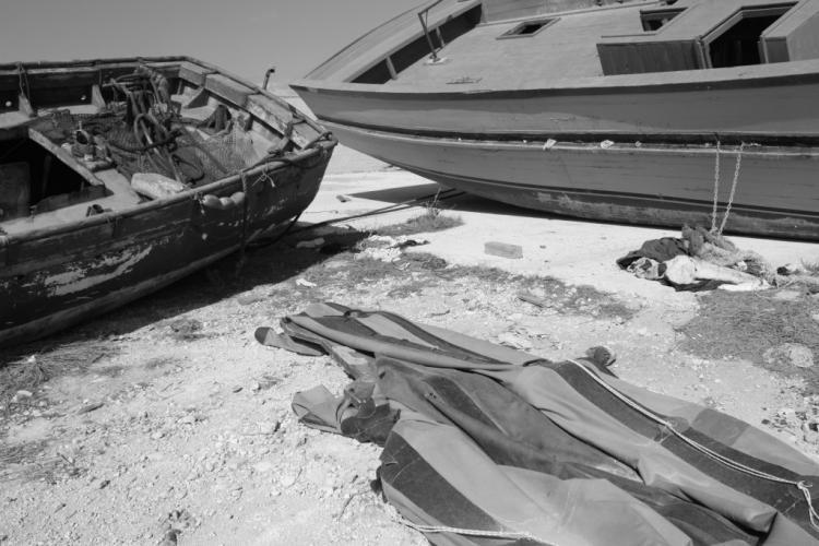 bordering in cultural productions in Europe. On the cliffs overlooking the Mediterranean, wooden fishing boats rest on the ground, monumental and silent.