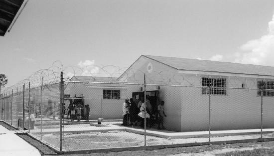 19 BAHAMAS Forgotten Detainees? Human Rights in Detention Photo of huts at Carmichael Detention Centre surrounded by internal barbed wire fence.