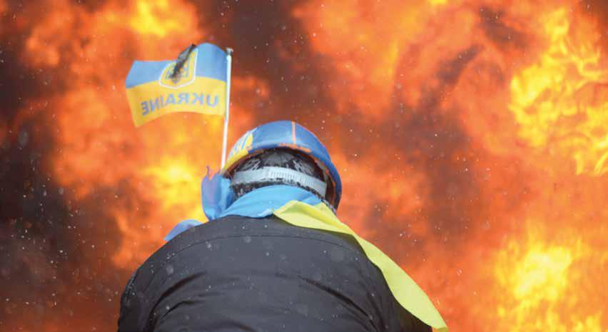 Demonstrator wearing Ukraine state flag colors facing the massive fire set by protesters to prevent internal forces from crossing the barricade line; Kyiv, Ukraine (January 22, 2014).