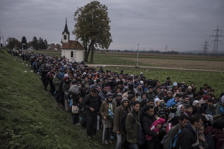 Oct. 22, 2015. Migrants walking past a church, escorted by Slovenian riot police to a registration camp outside Dobova, Slovenia.