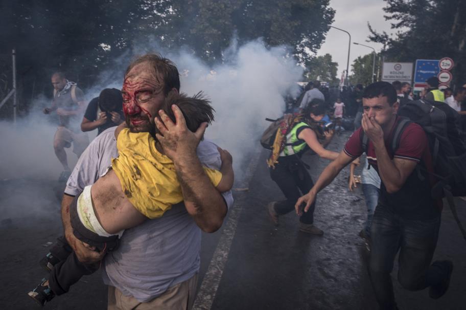 Sept. 16, 2015. A man tries to shield his child from police beatings and tear gas at the border crossing in Horgos, Serbia.