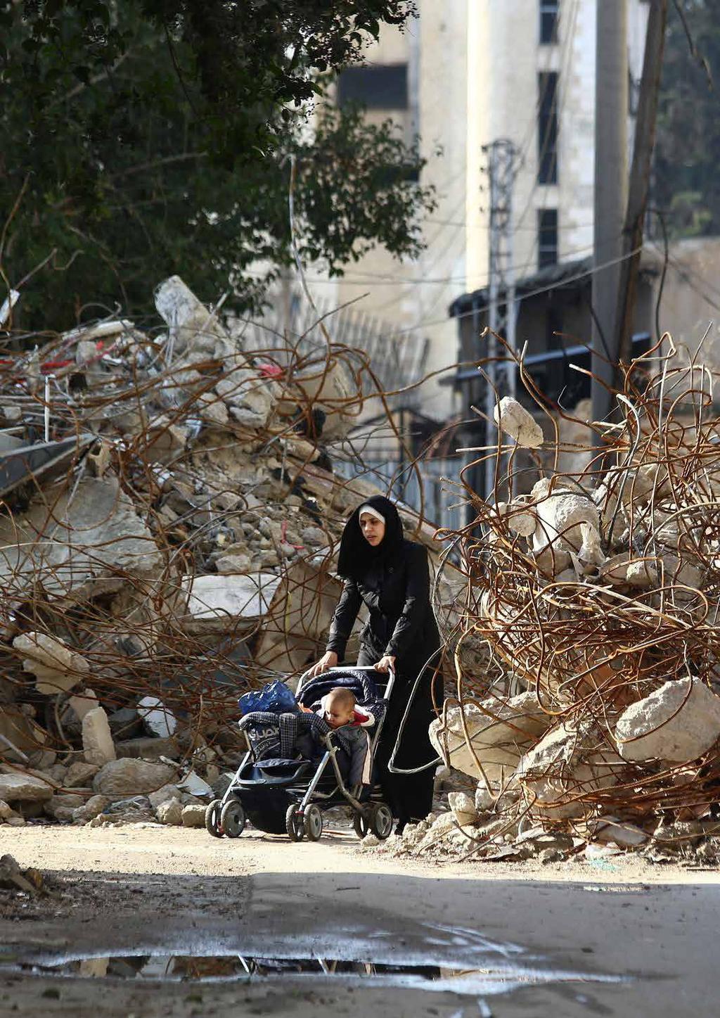 A woman walks pushing a pram between the rubble of destroyed buildings in the besieged rebel bastion of Duma on December 13 2014.