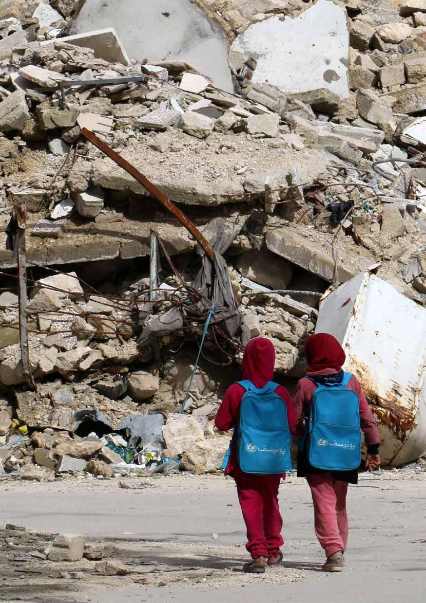 Syrian girls, carrying school bags provided by UNICEF, walk past the rubble of destroyed buildings on their way home from