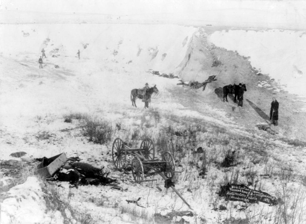 Photograph of the aftermath of the massacre at Wounded Knee. The bodies of Sioux who lost their lives are visible in the foreground and along the ridge. Image courtesy Wikimedia Commons.