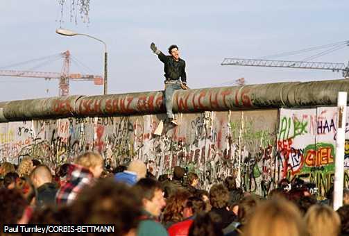 Cheering the End of the Berlin Wall A man sitting on the Berlin Wall, which divided East and West Germany from 1961 to 1989, raises a fist and cheers the dismantling of the wall.