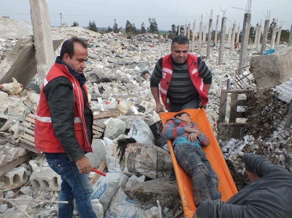 Image showing Kurdish Red Crescent rescue teams trying to evacuate a child stuck under wreckage after warplanes attacked a poultry farm near the village of Anabke in Afrin suburbs where IDPs were