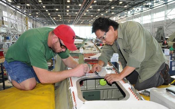 Machinists Lonnie Conditt (left) and Narom Orr measure holes to ensure alignment with the Y497 former positioned below the dorsal deck of an F/A-18 Hornet on the production line at Fleet Readiness