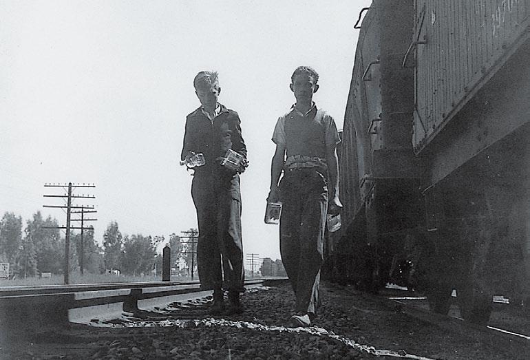 Two young boys, ages 15 and 16, walk beside freight cars in the San Joaquin Valley. Many teenagers looked for a way out of the suffering or to ease the pressure on their families.