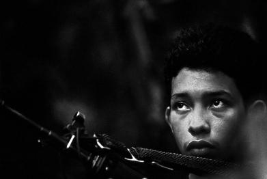 A fifteen year old, after three months of training, on his first day of active military duty as a FARC guerrilla guards a jungle camp in the state of Caquetá, Colombia, 2000.
