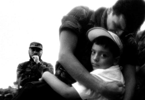 A soldier hugs his son who he has not seen for 3 years as a guerrilla commander looks on during a POW release ceremony in La Macarena, Colombia in 2002.
