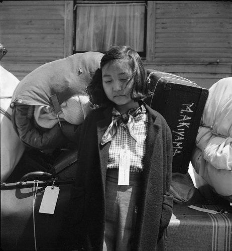Oakland, California. A young evacuee guards the family baggage prior to departure to an assembly center.