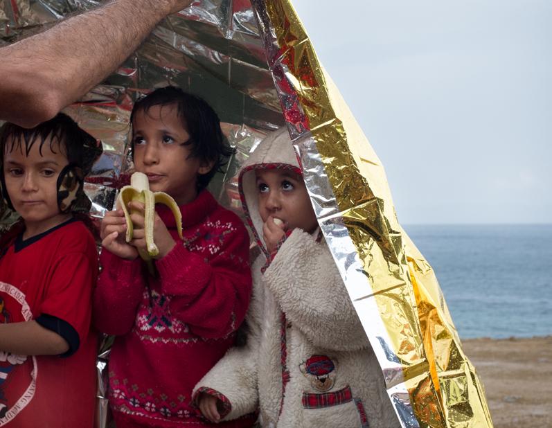 Unicef/Gilbertson ARRIVING BY SEA: GREECE PHOTO SHEET 5 Three child refugees shelter beneath an emergency blanket.